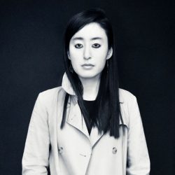 Black and white headshot of Visiting Fellow R. O. Kwon. She is looking at the camera in front of a black background. Her long black hair is down and she is wearing a black top with a white collared coat.